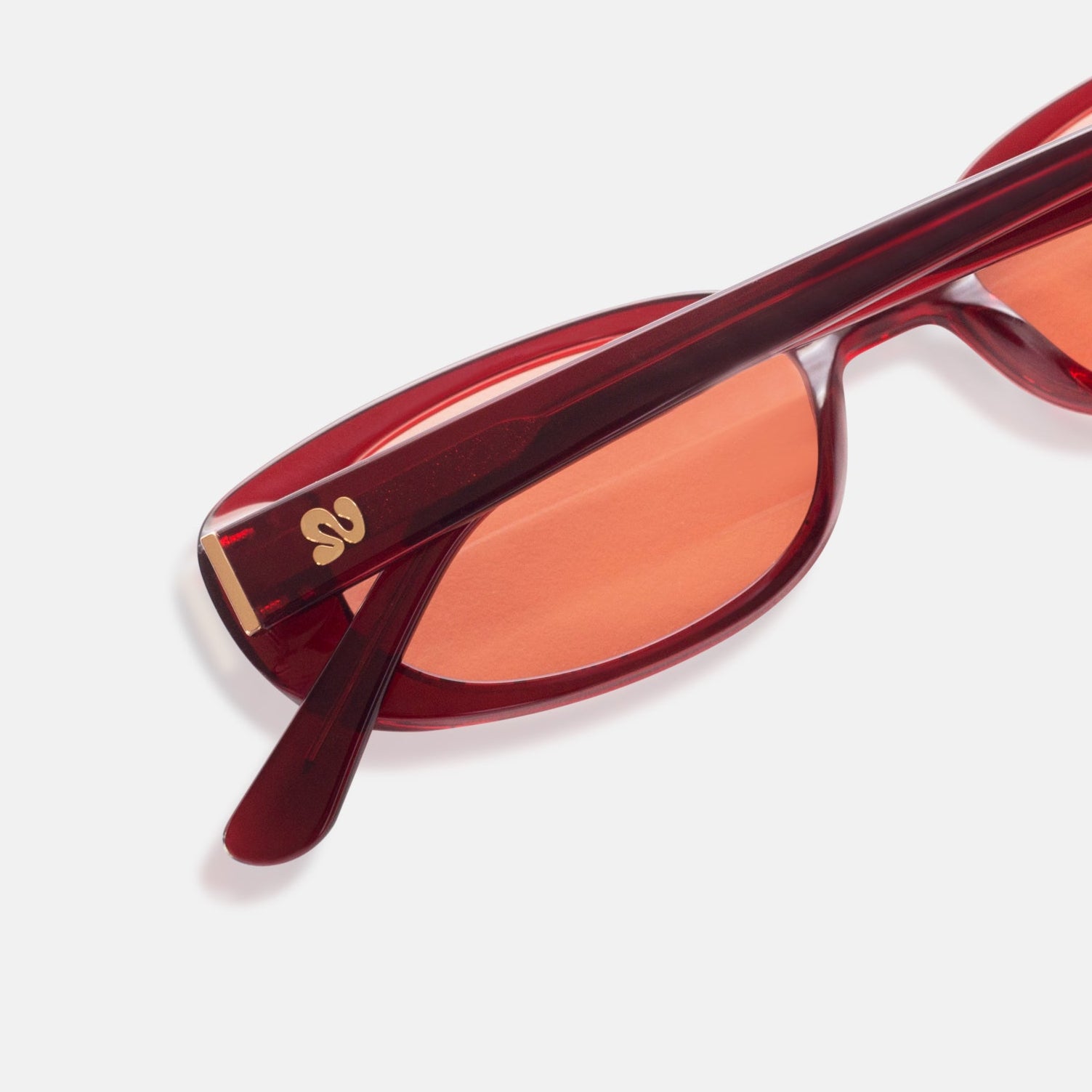 Close-up of Isla Sunwear logo on cherry red rectangular sunglasses, designed for smaller faces.