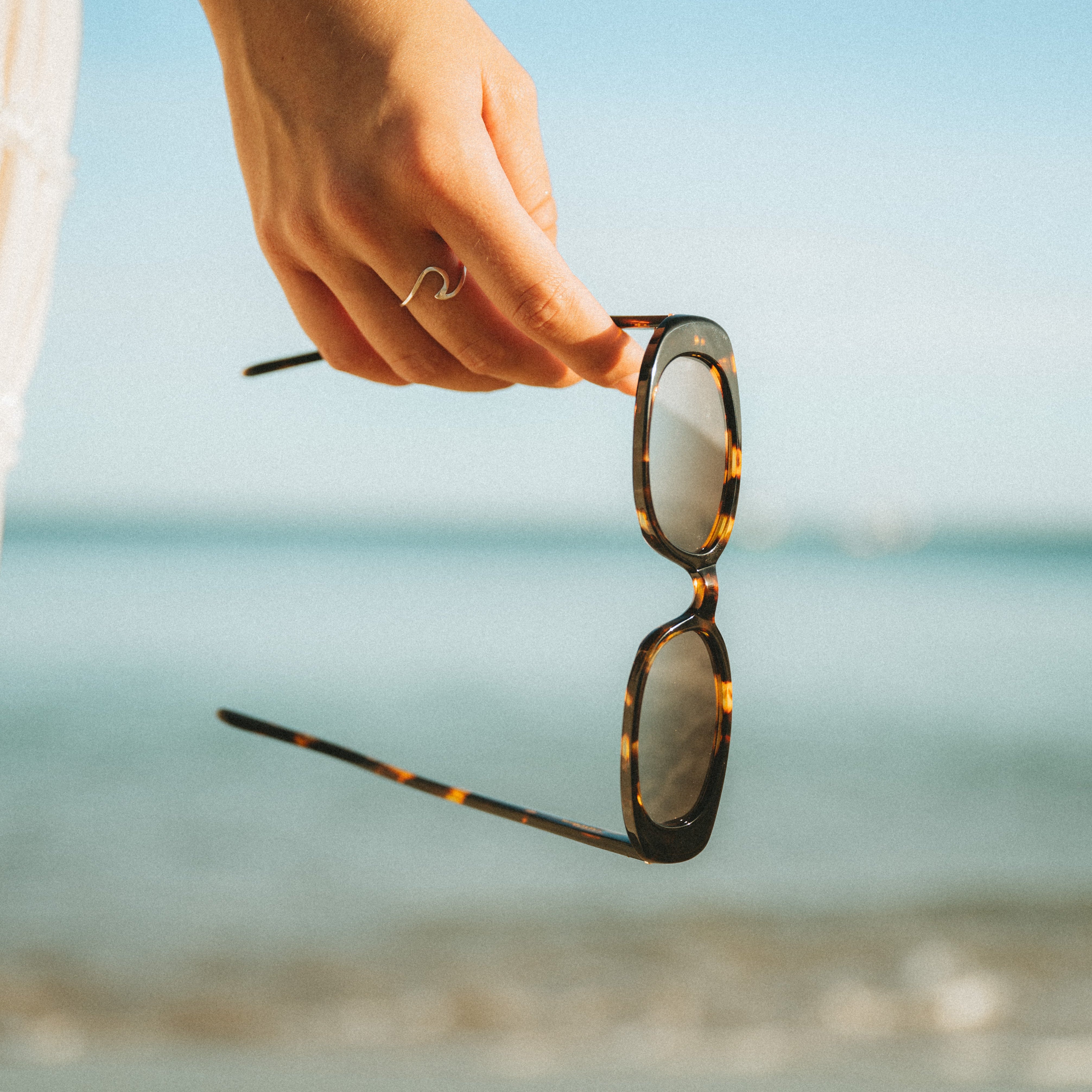 Closeup product shot of a woman holding Isla Sunwear tortoise oval sunglasses, designed for smaller faces.