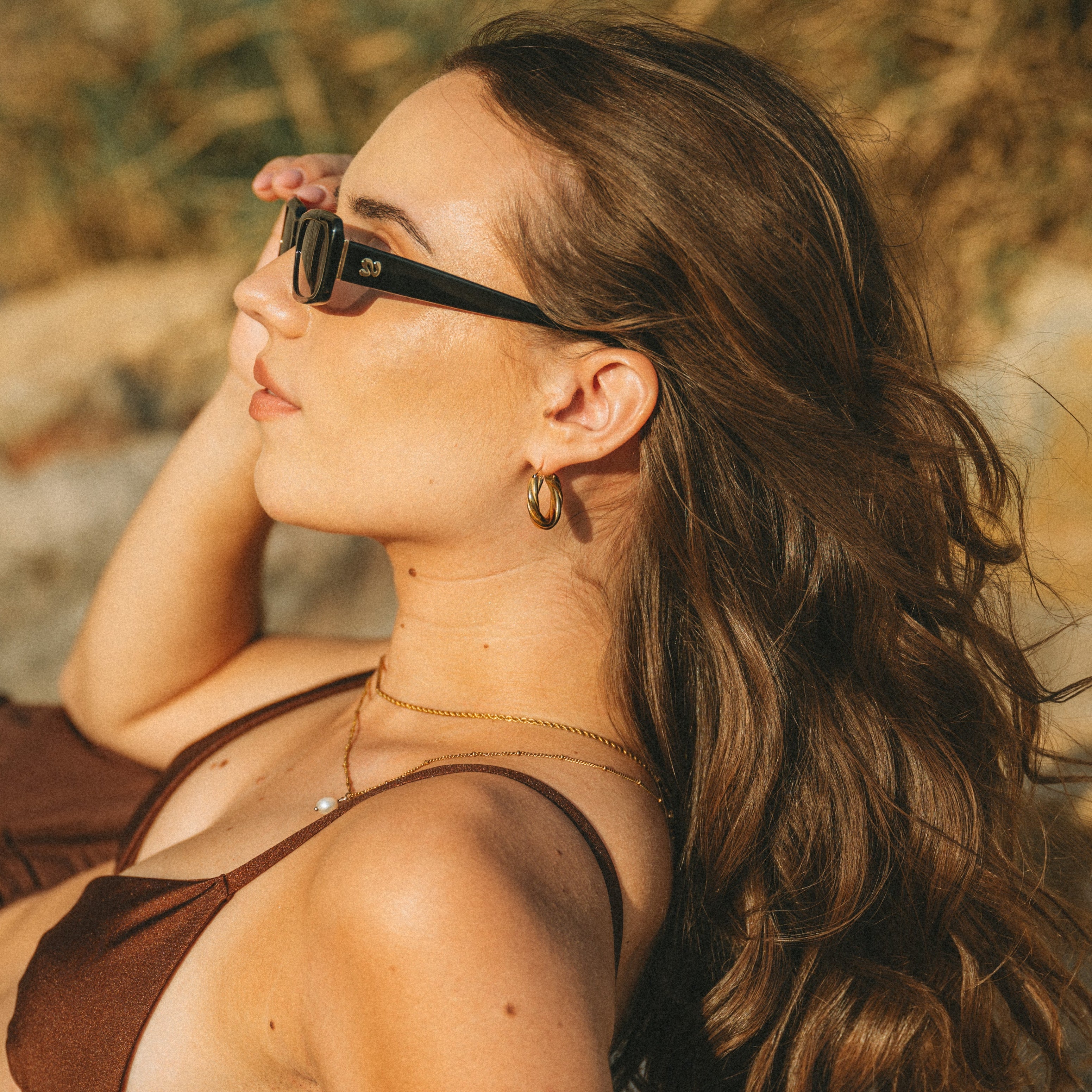 Golden-hour beach portrait side view of woman wearing Isla Sunwear black rectangular sunglasses, designed for smaller faces.
