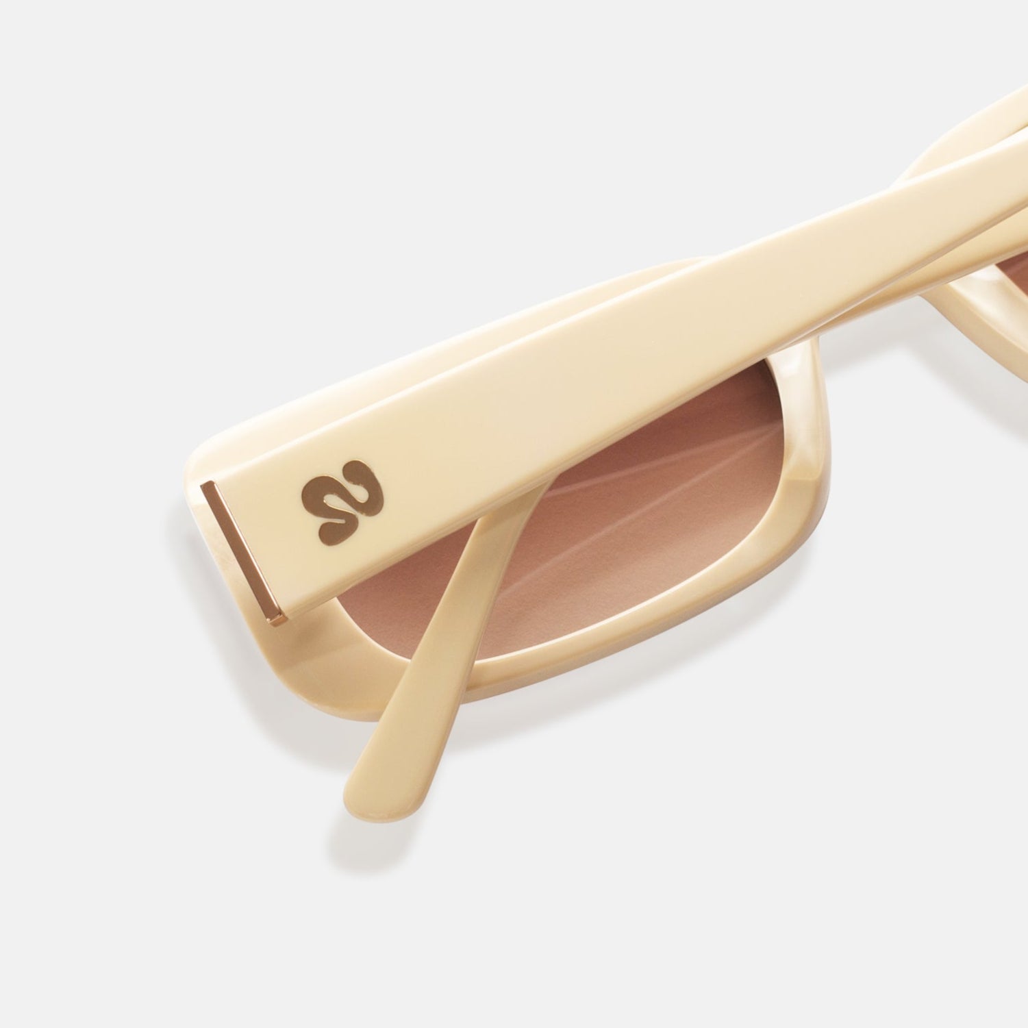 Close-up of Isla Sunwear logo on sand-colored rectangular sunglasses, designed for smaller faces.