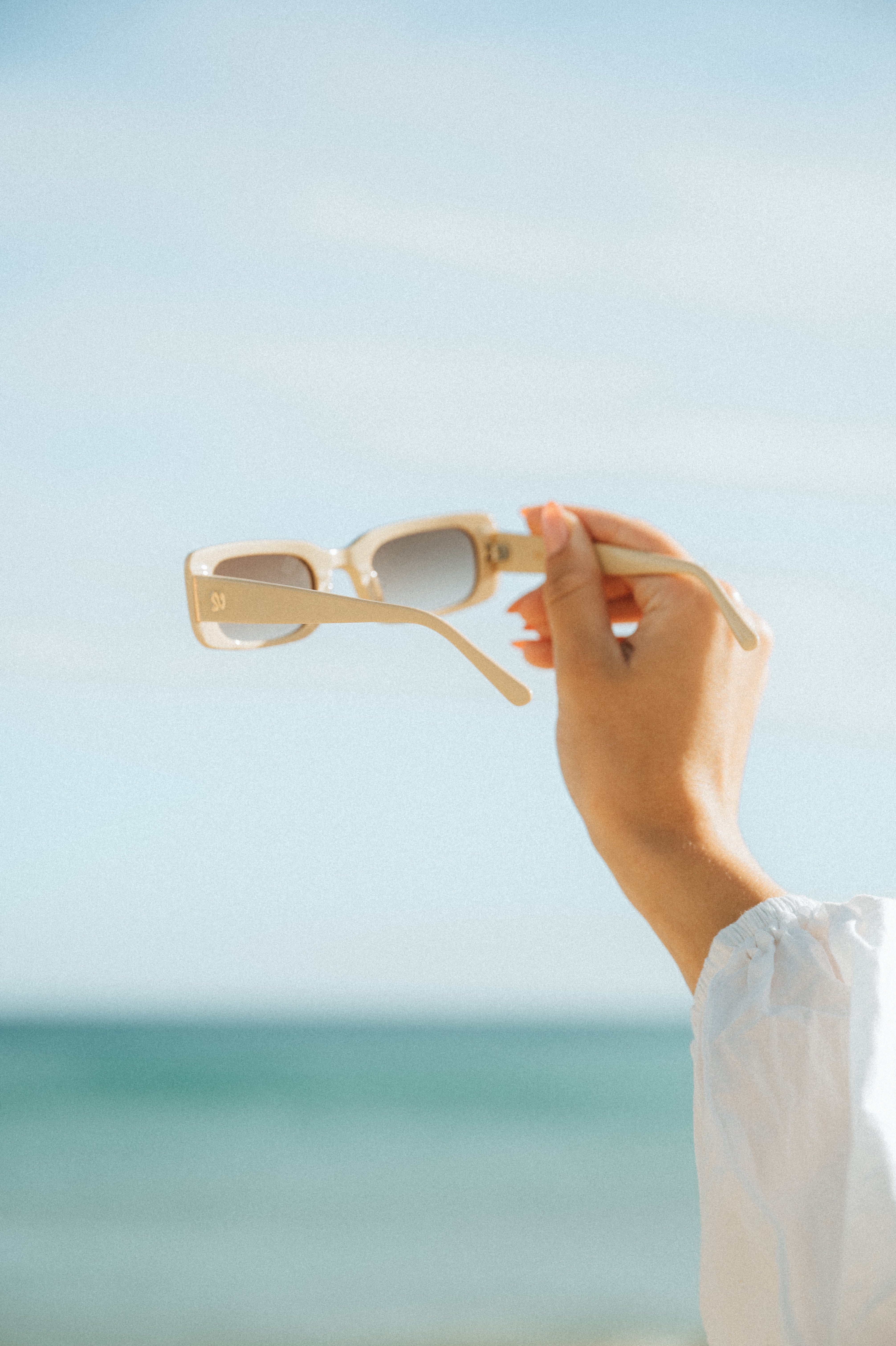 Product shot of a woman holding Isla Sunwear sand rectangular sunglasses, designed for smaller faces.