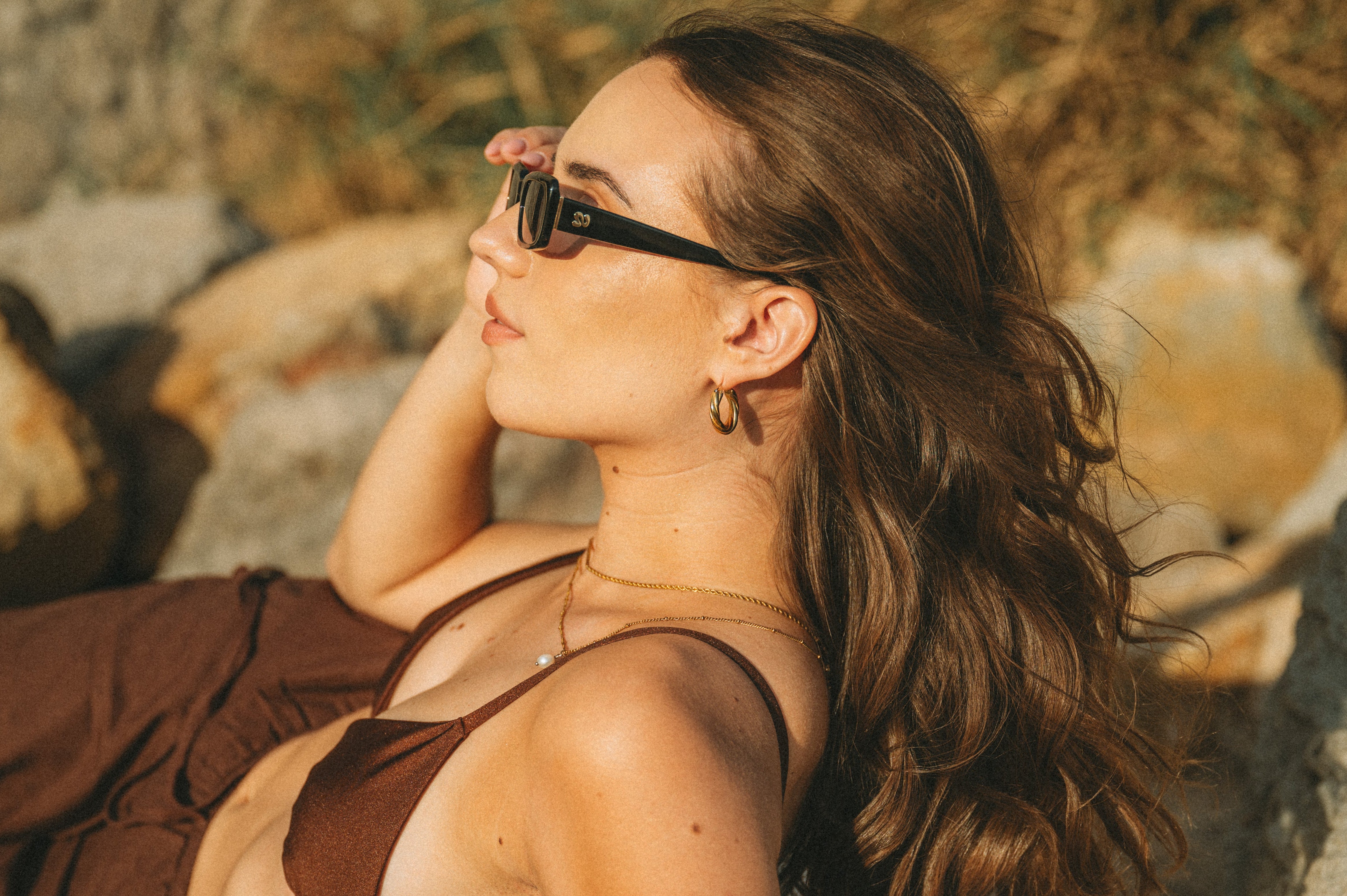 Golden-hour beach portrait side view of woman wearing Isla Sunwear black rectangular sunglasses, designed for smaller faces.