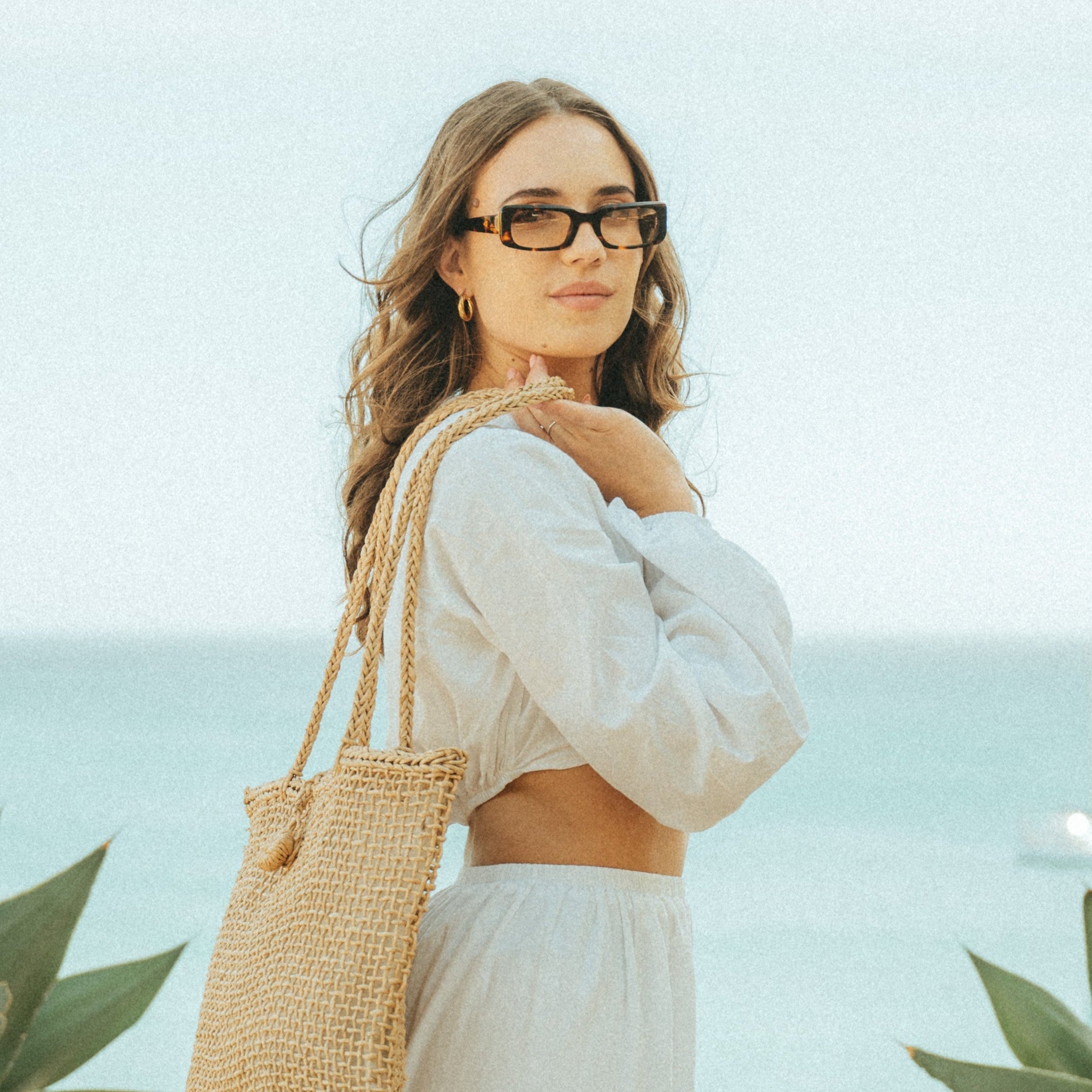 portrait of a woman with a beach bag wearing Isla Sunwear tortoise rectangular sunglasses, designed for smaller faces.